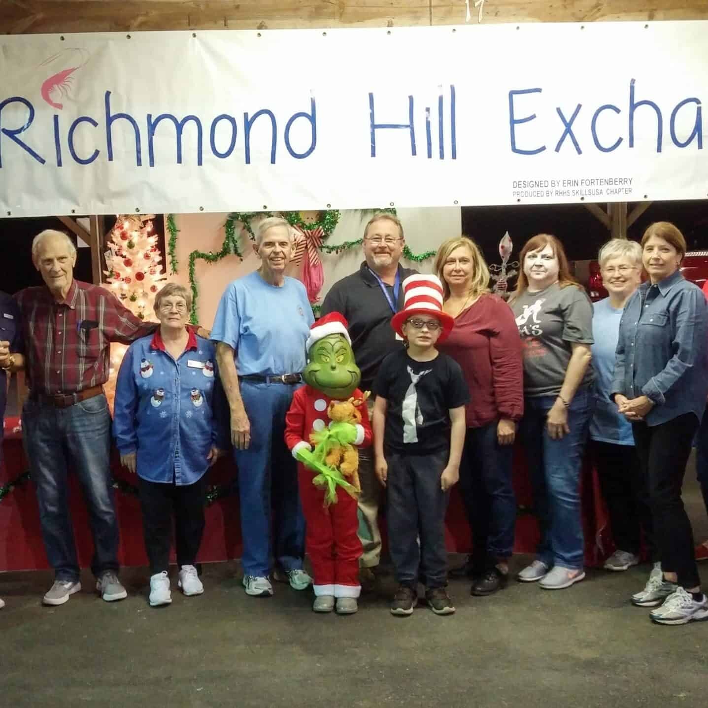 Two children dressed in Doctor Seuss costumes with eight men and women standing behind them under an Exchange Club banner with Christmas decorations in the background