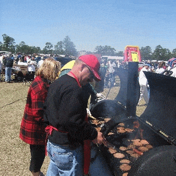 People manning hamburgers cooking on two barrel grills