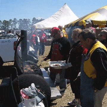 A woman and two men tending to hamburger patties on the barrel cooker grills