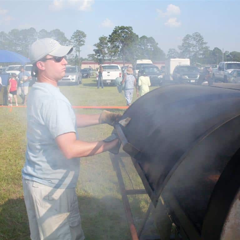 Man tending to a barrel cooker with smoke billowing out of it