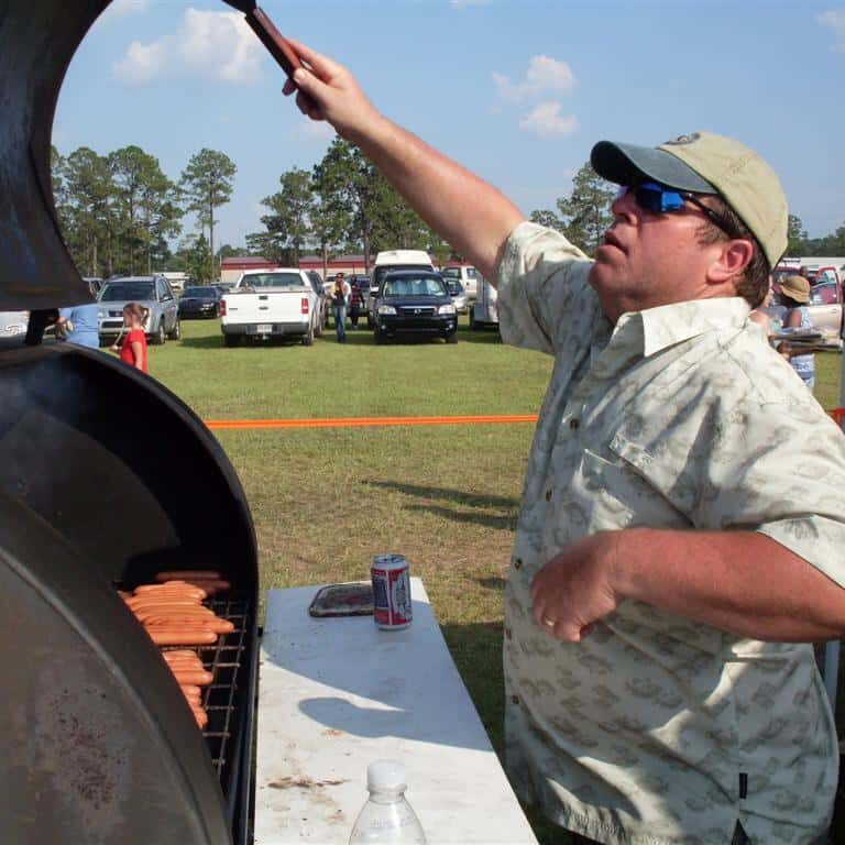 Man tending to hotdogs on a barrel cooker grill