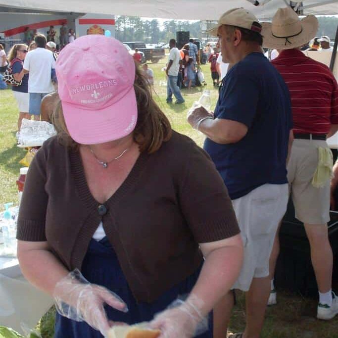 A woman in a pink New Orleans cap is preparing hot dogs while two men take food orders from customers