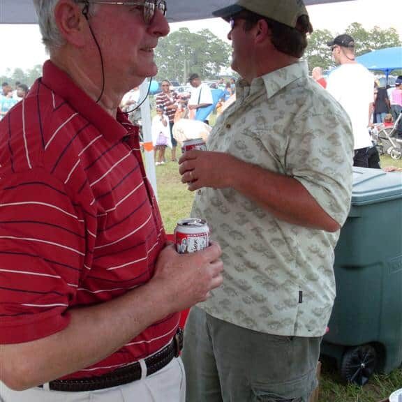 Two men enjoying cans of beer under a food vendor tent