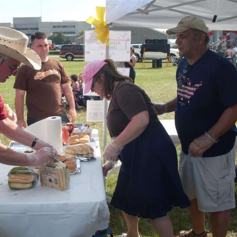 A woman and two men wearing food safety gloves serving hot dogs