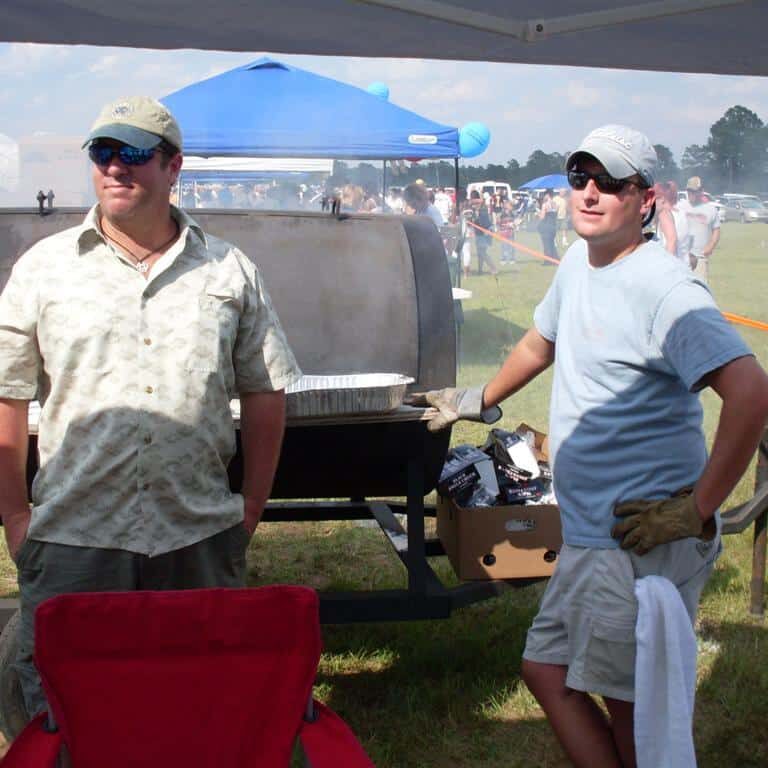 Two men attending a barrel smoker outdoors