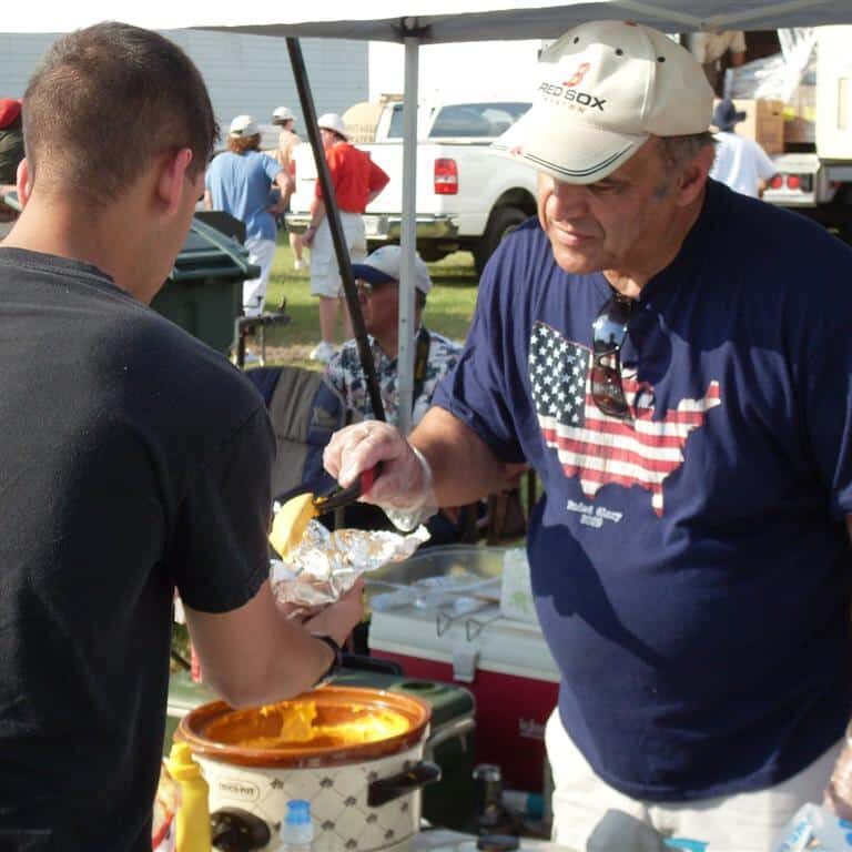 A man wearing a patriotic T-shirt is serving a younger man food from a crockpot