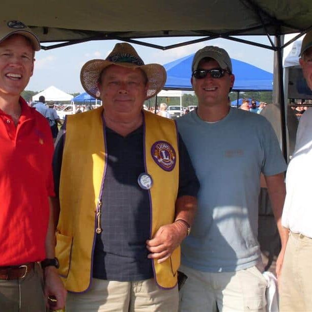 Four male Lions Club members standing under a food tent