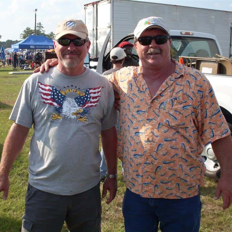 Two men posing in front of a white pickup truck loaded with folding chairs