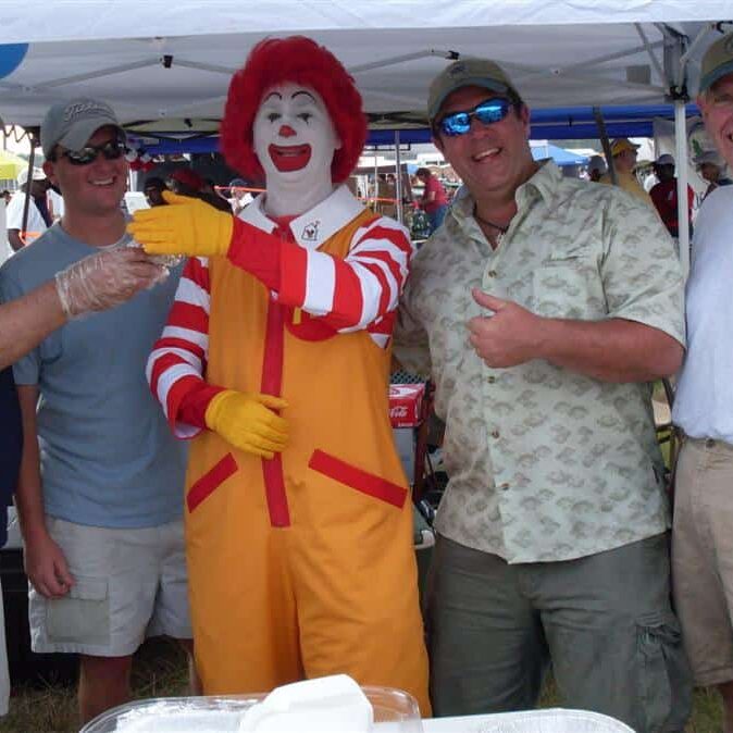 Four men under a food tent laughing it up with the Ronald McDonald House clown mascot