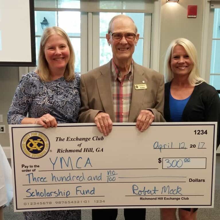 Two women standing on either side of an Exchange Club presenter holding a large ceremonial check made out to the YMCA in the amount of three hundred dollars