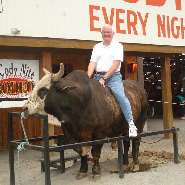 Senior man sitting on a live bull that is tethered to railing