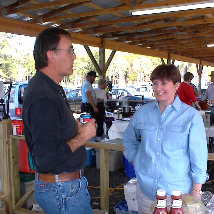 Man and women conversing behind a condiment table under a pavilion