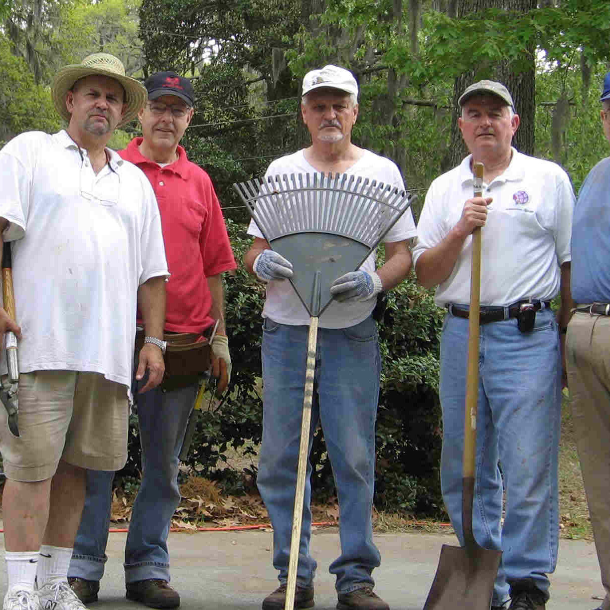 Five men holding lawn and garden tools standing outside