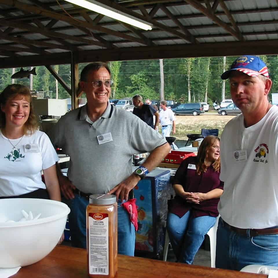 Three smiling people under a pavilion preparing to fry fish