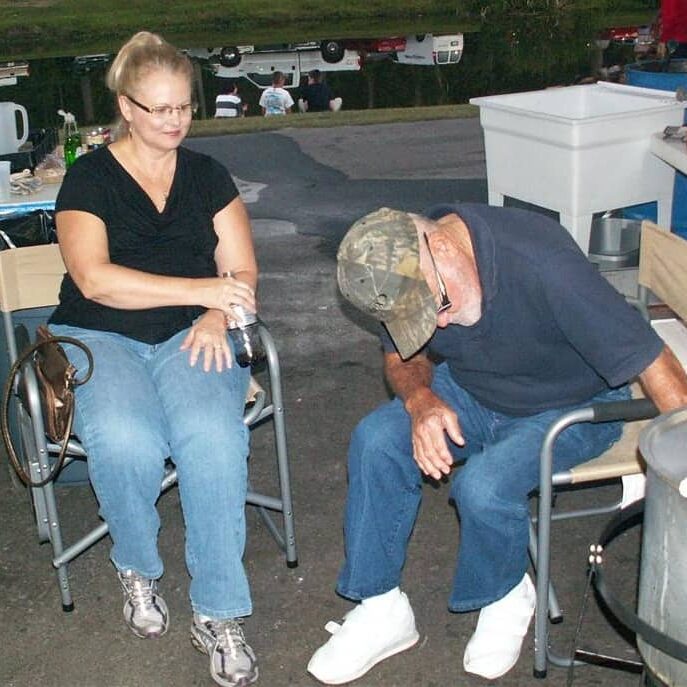 A woman and man in folding camping chairs tending to a large aluminum pot