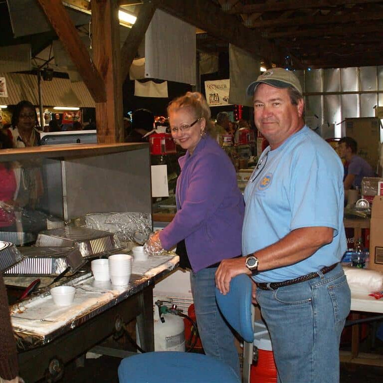 A smiling man and woman dishing up food from large aluminum pan trays