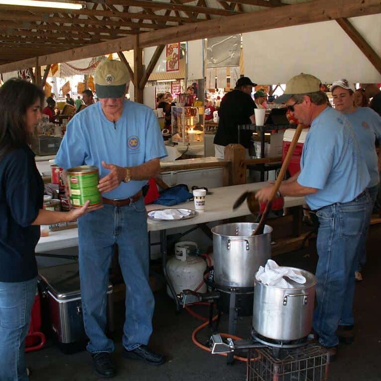 Three Exchange Club members tending to two large aluminum pots on a propane cooker