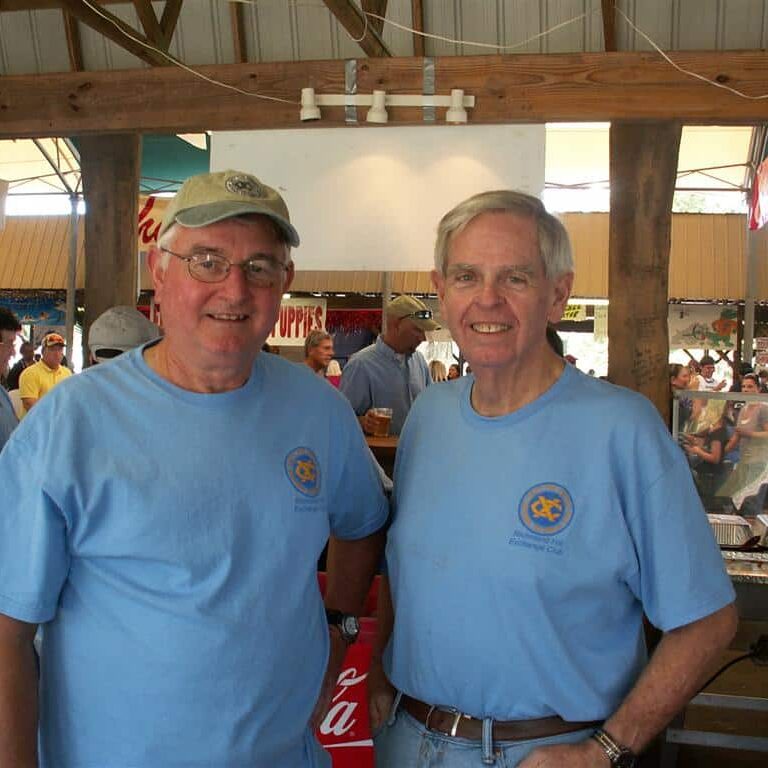 Two men wearing Exchange Club T-shirts at a food stall