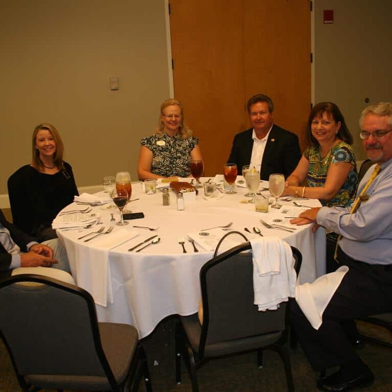 A group of six men and women seated at a round banquet table