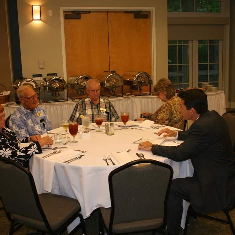 Five men and women conversing while seated at a round banquet table