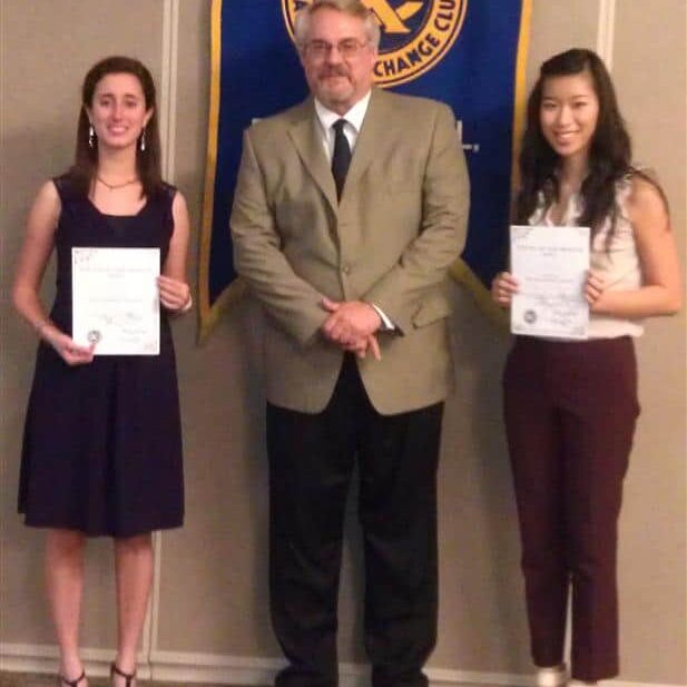 A male Exchange Club member flanked by two female students holding certificates