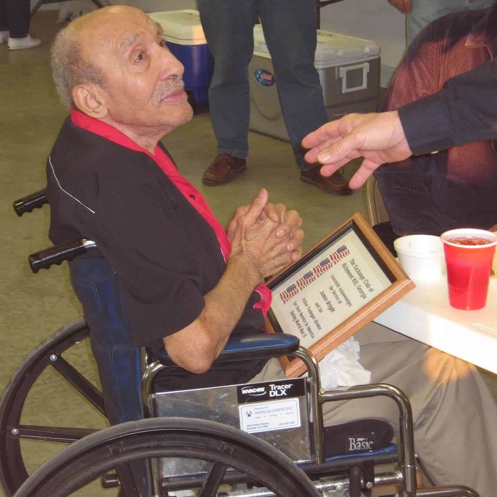 Mr. James Wright in his wheelchair holding the framed military service appreciation he was presented with earlier