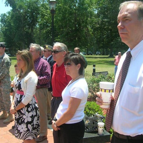 A group of adults, some in military uniforms, attending an outdoor ceremony