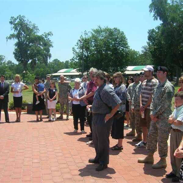 A diverse audience standing at an outdoor veterans memorial ceremony