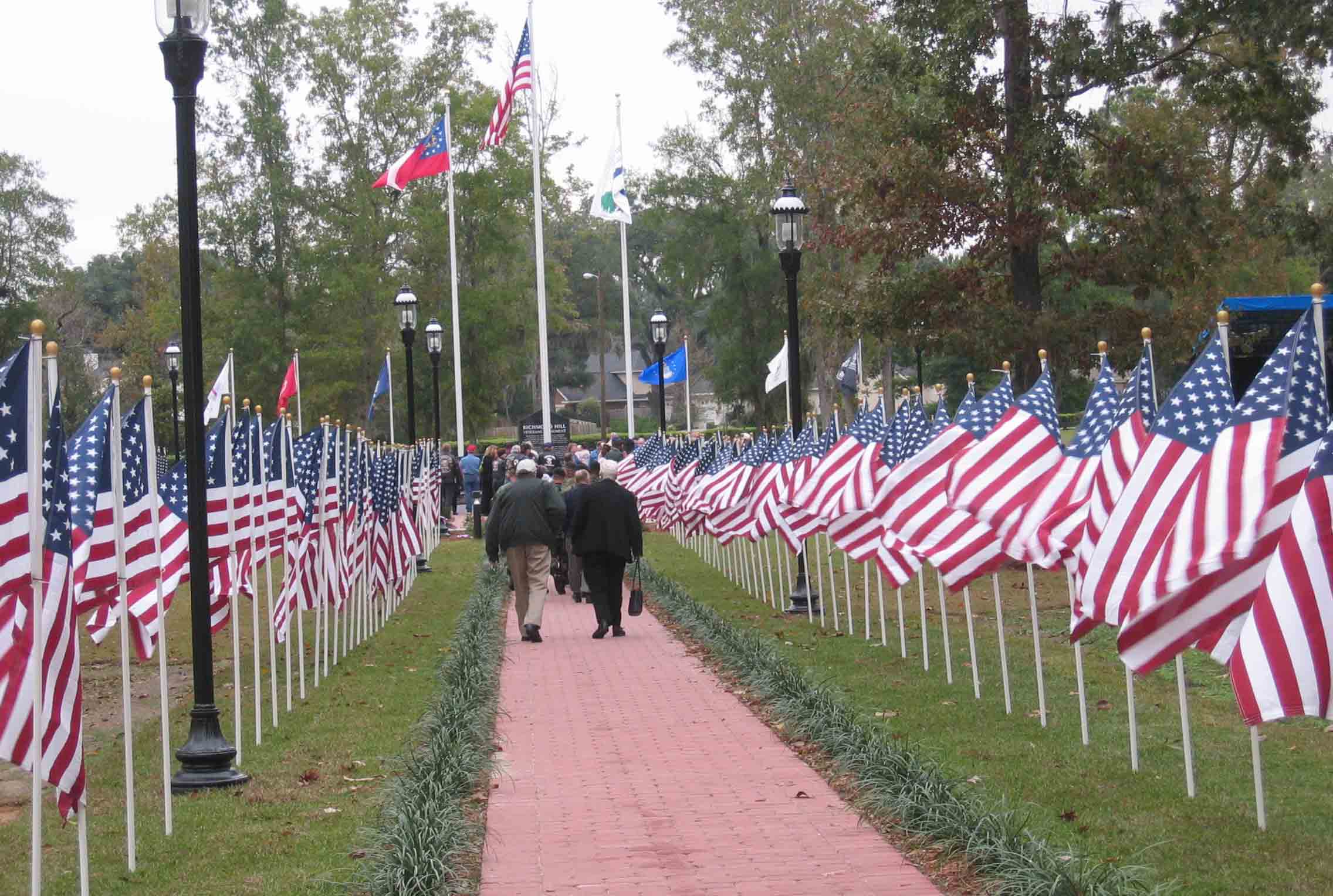 People on a brick walkway flanked by American flags as they make their way to the ceremony